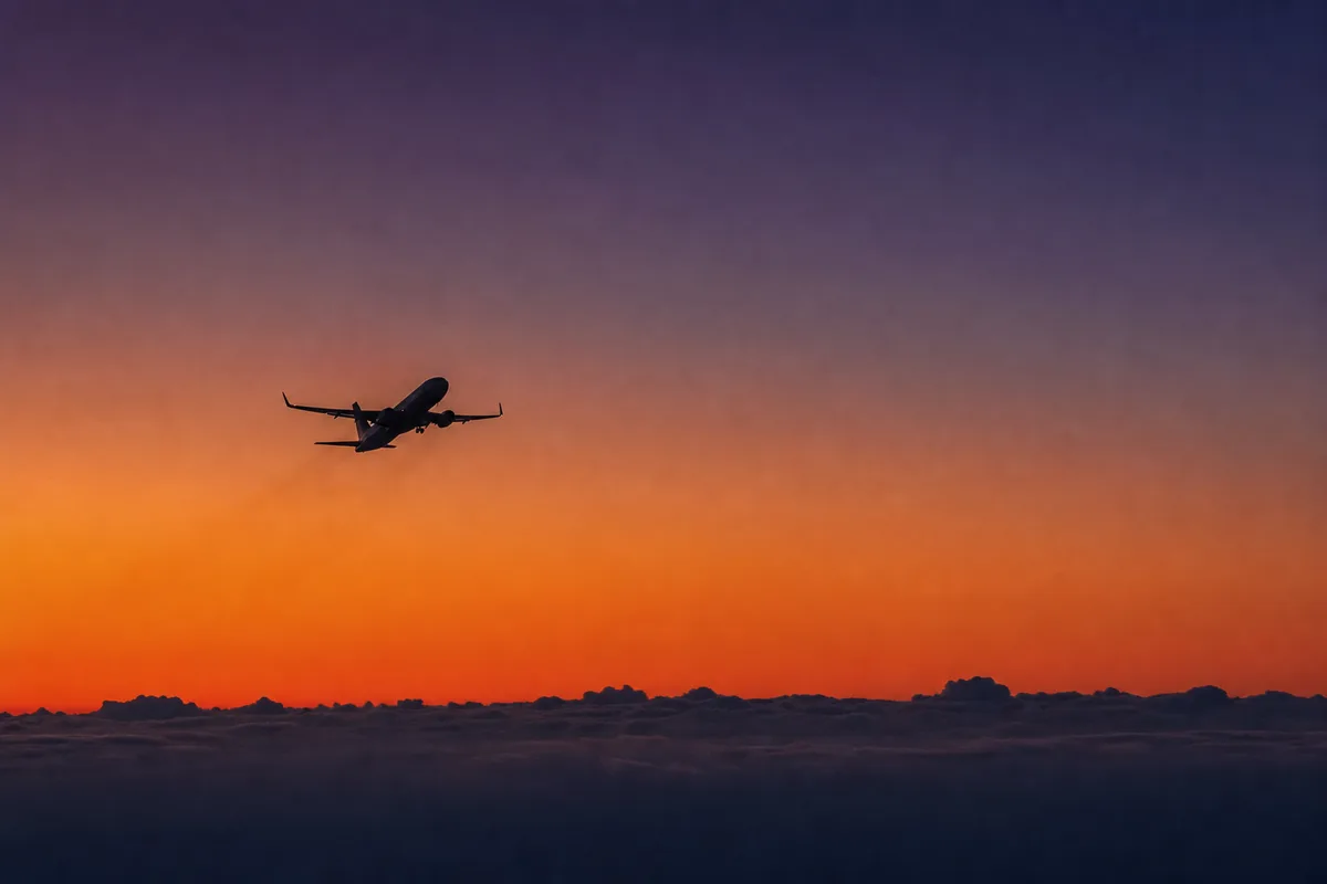 Silhouette d’un avion de ligne en montée initiale à contre-jour dans un ciel de crépuscule orangé