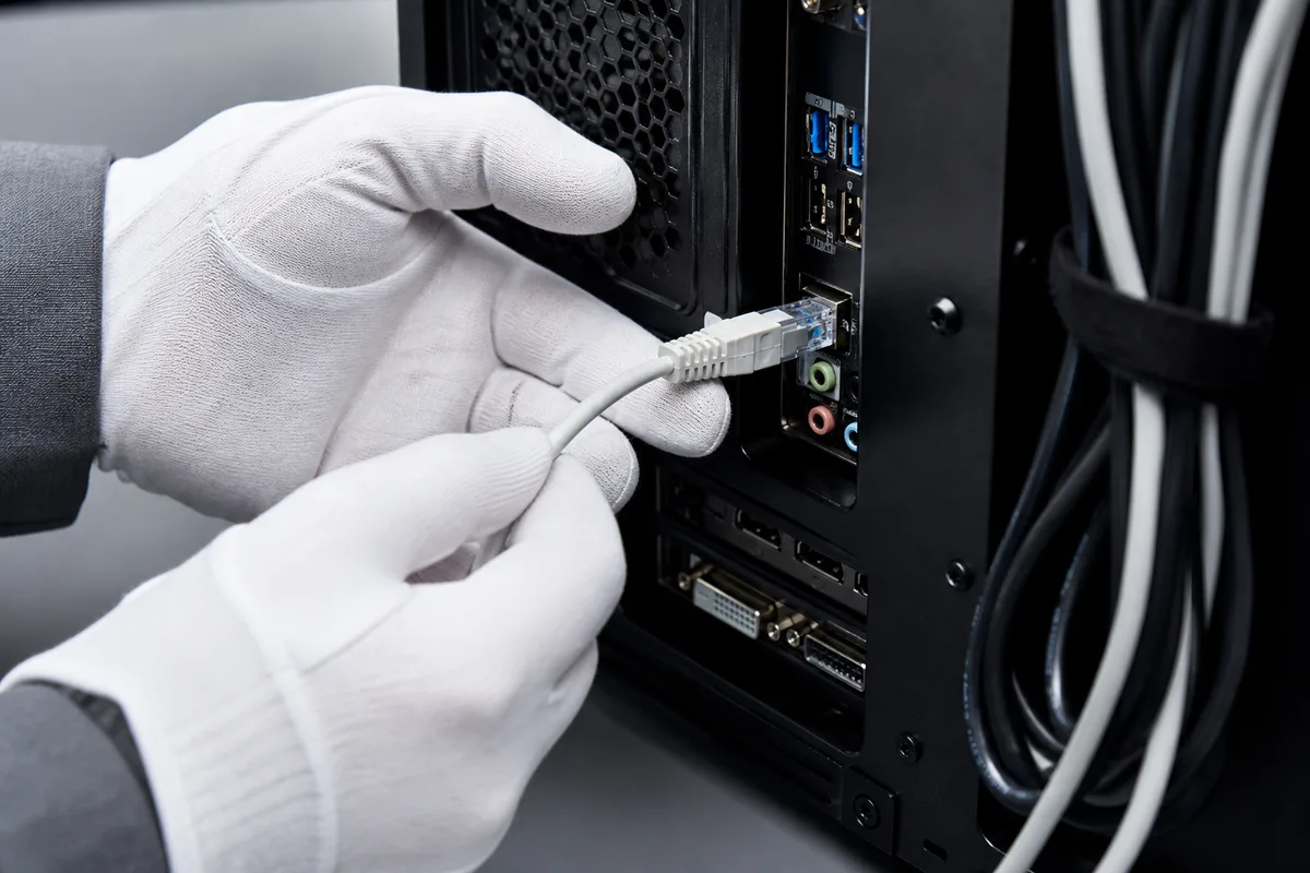 Technicien vérifiant la connectique arrière d’un ordinateur fixe posé sur un plan de travail