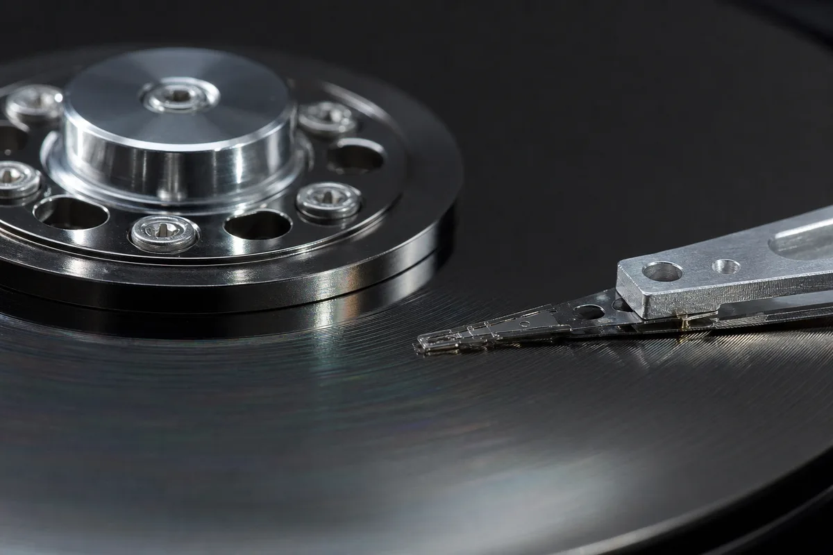 Disque dur mécanique ouvert en macro, plateaux et bras de lecture visibles sur un plan de travail
